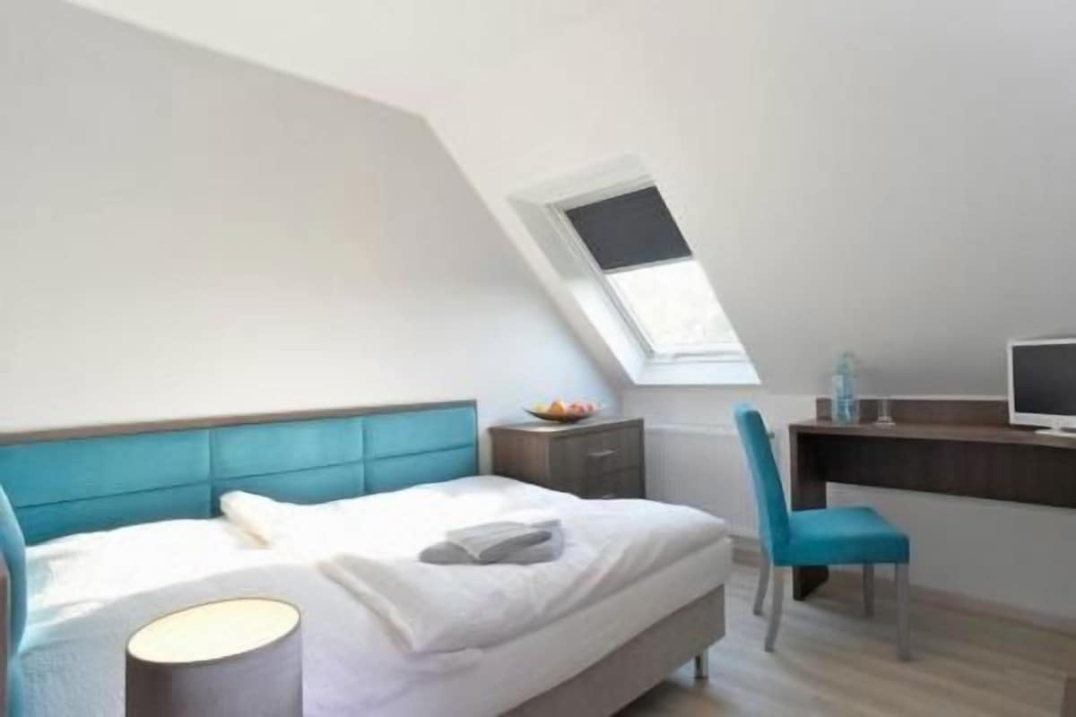 Un dormitorio con cama, mesita de noche, silla, escritorio y ventana.