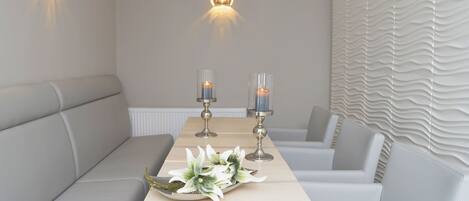 A modern dining area with a long table, two wall-mounted light fixtures, and a decorative centerpiece.