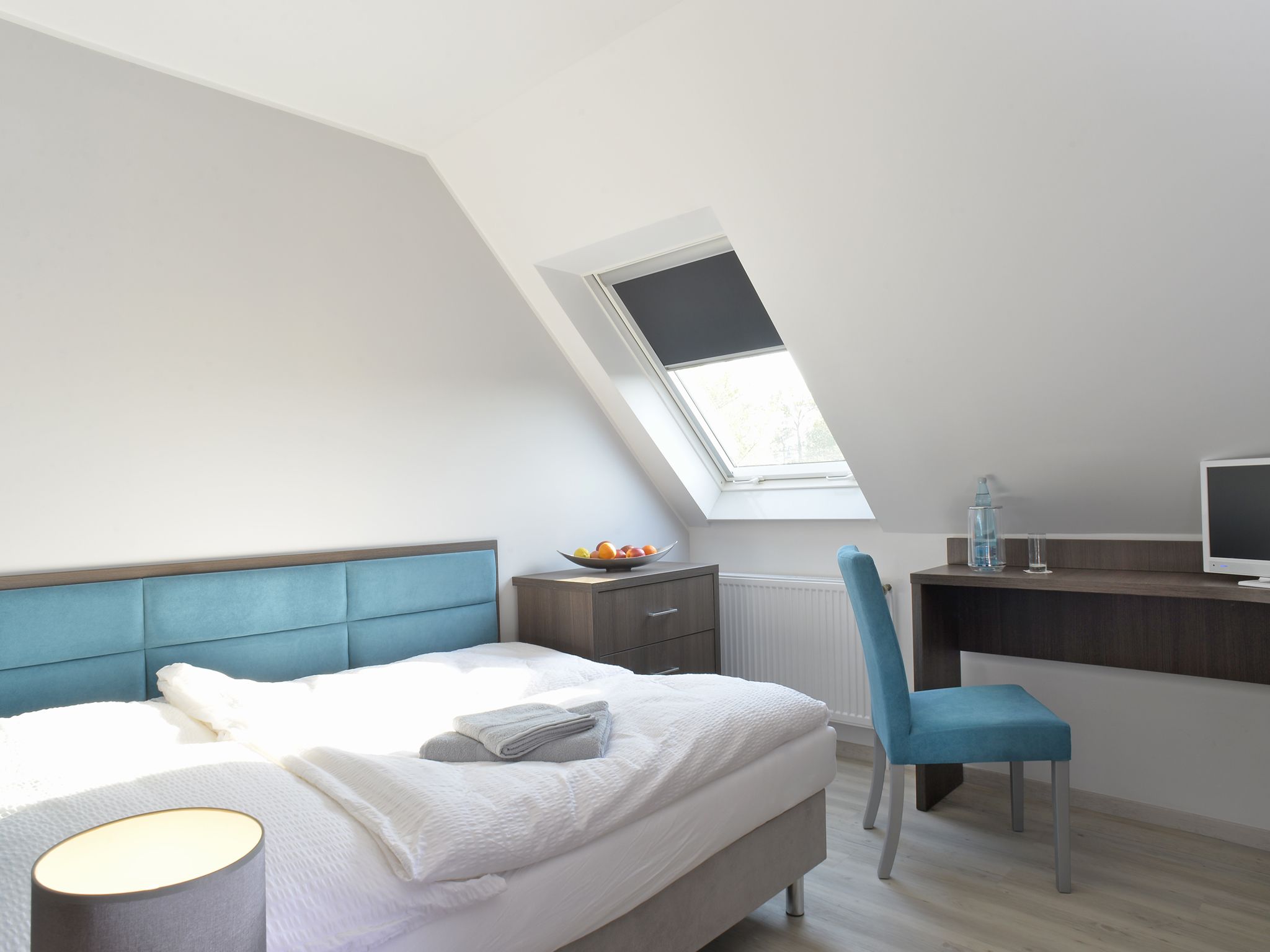 A bedroom with a bed, a desk, a chair, a TV, and a skylight.