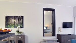 Una sala de estar moderna con comedor, un espejo grande, un televisor de pantalla plana y una escalera que lleva a otra habitación.