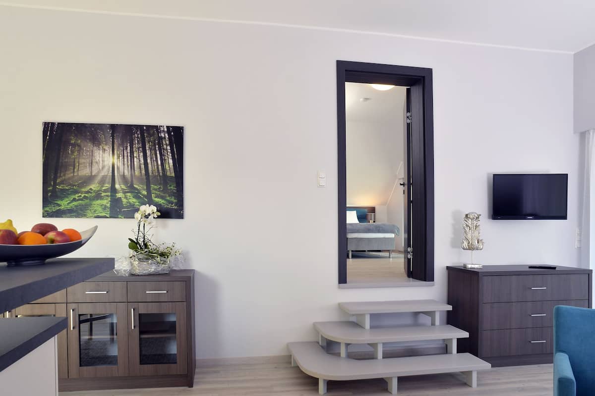 Een moderne woonkamer met een eethoek, een grote spiegel, een flatscreen televisie en een trap naar een andere kamer.