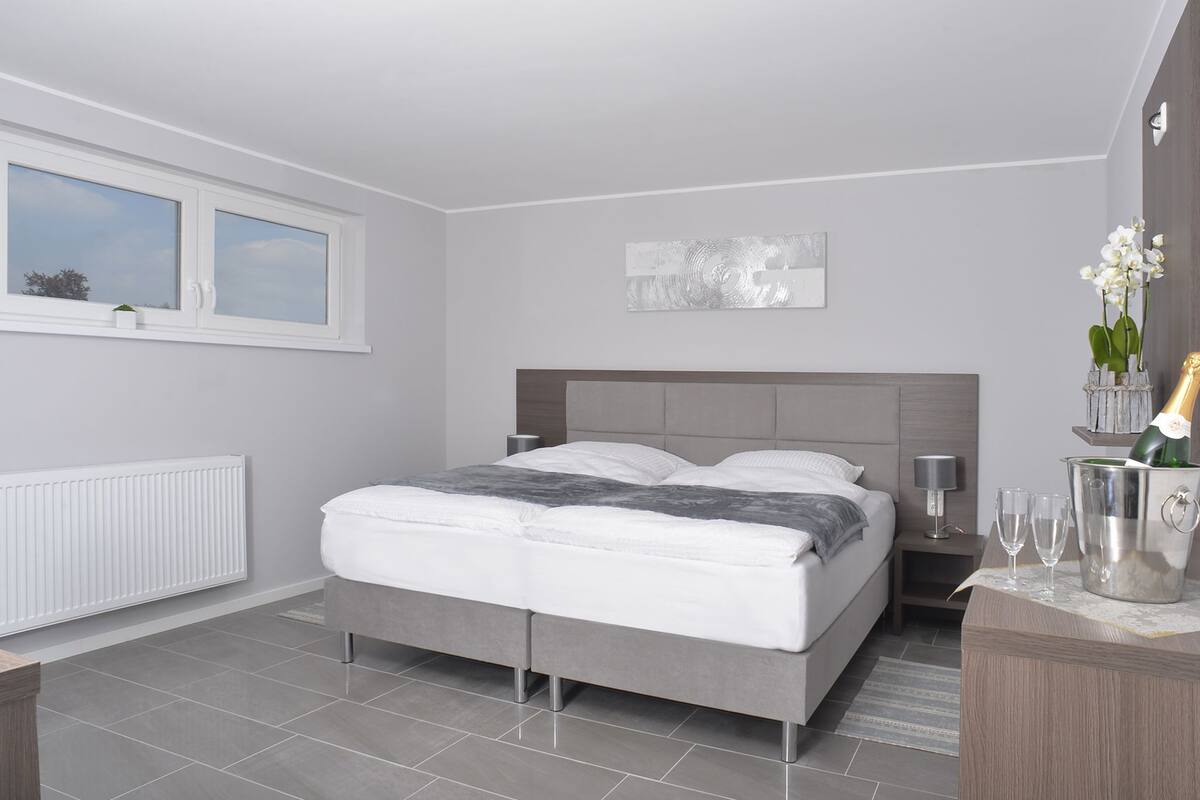 Een moderne slaapkamer met een bed, nachtkastjes, een radiator, een raam en een decoratief object aan de muur.