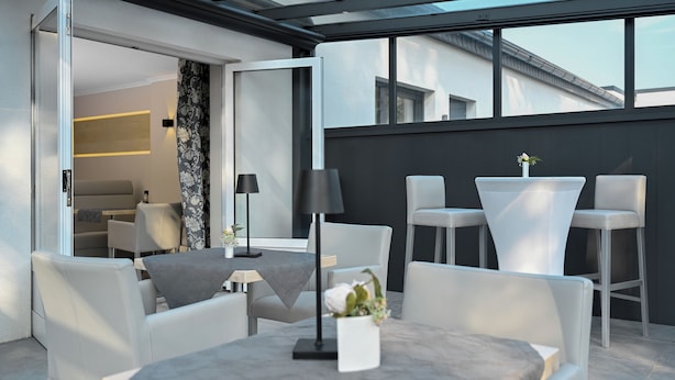 Un área de estar exterior moderna con sillas blancas, una mesa, una lámpara y un florero con flores.