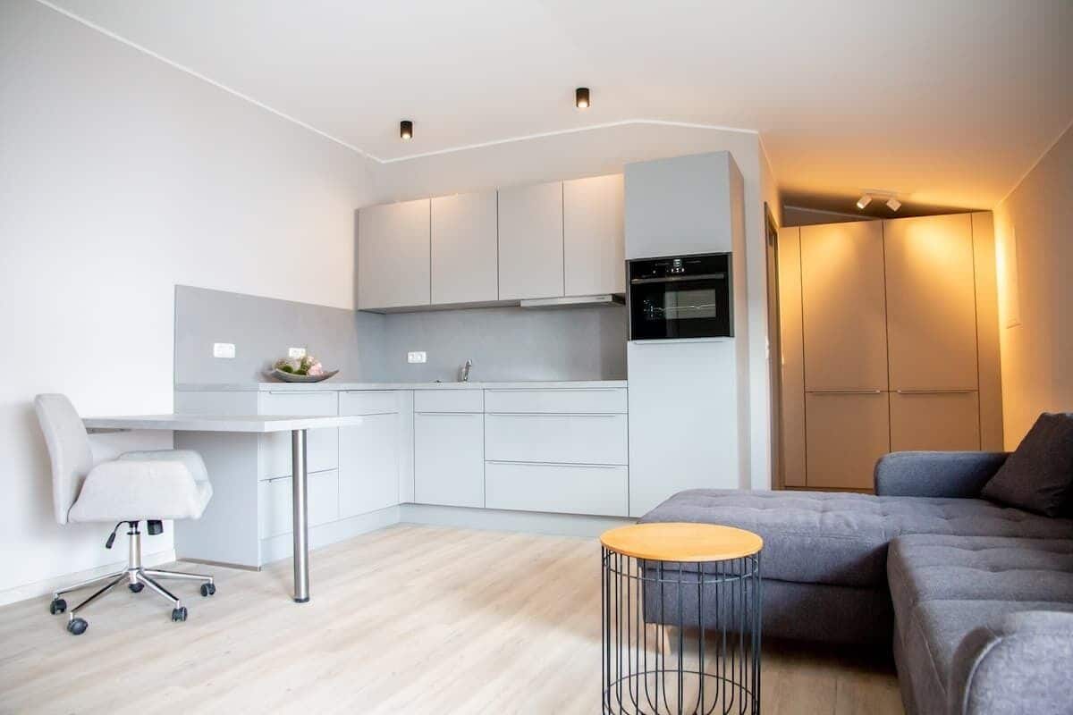 Een moderne keuken met witte kasten, een eethoek met een witte tafel en stoel, en een grijze bank in een compacte woonruimte.