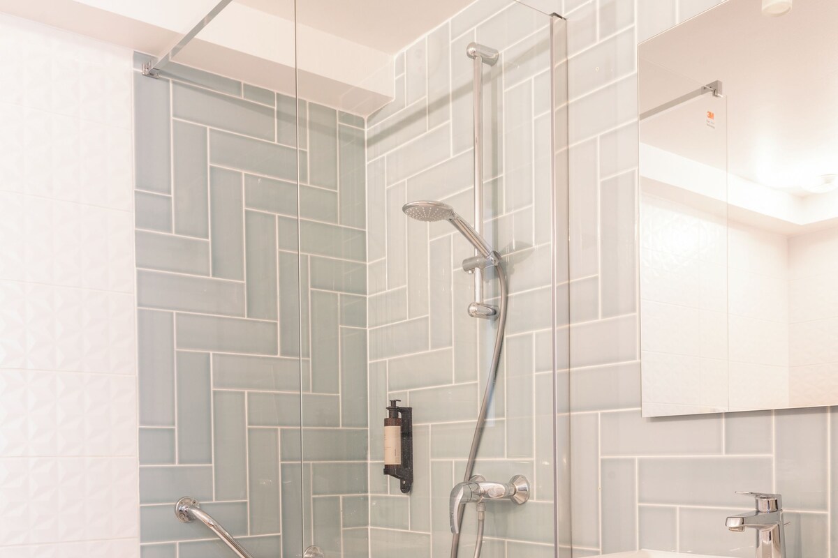 A modern bathroom with a glass-enclosed shower, a white sink, and a mirror above it.