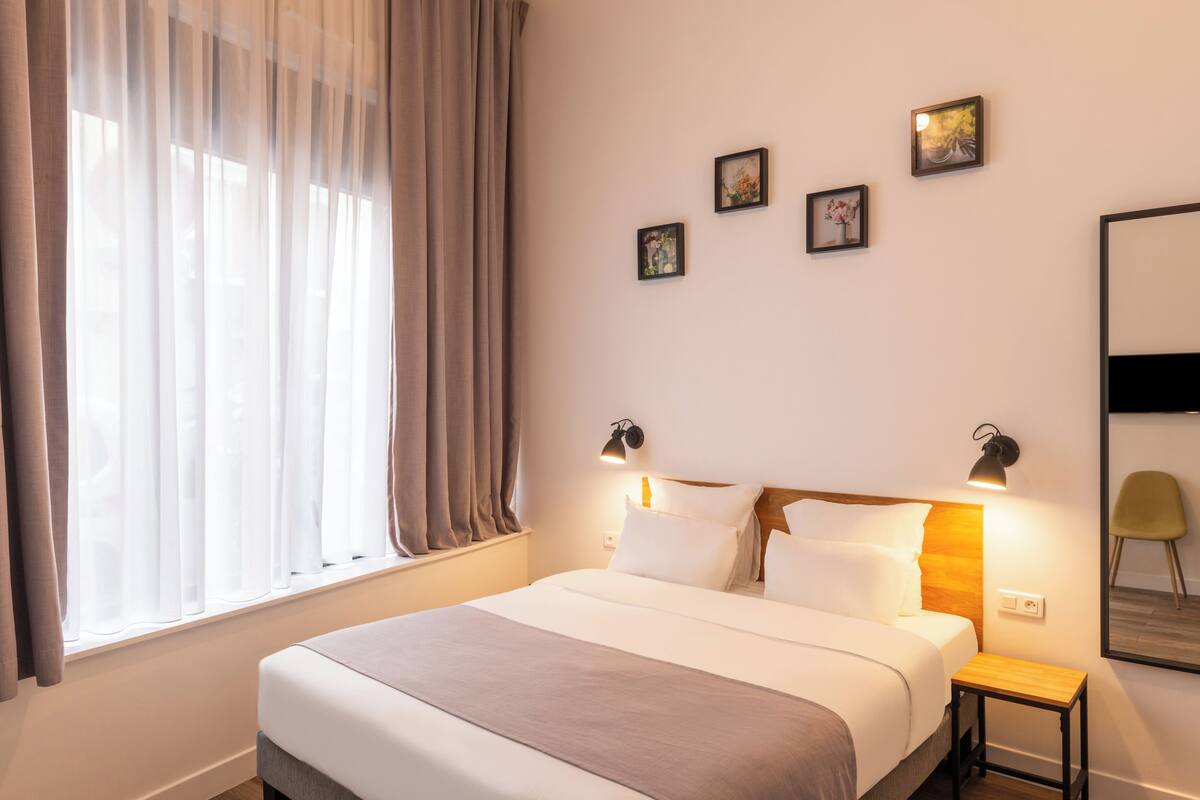 A neatly made bed with a wooden headboard, a bedside table, and wall-mounted lamps.