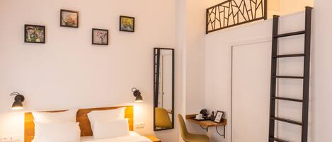 A hotel room with a bed, bedside lamps, a desk with a chair, a mirror, and framed pictures on the wall.