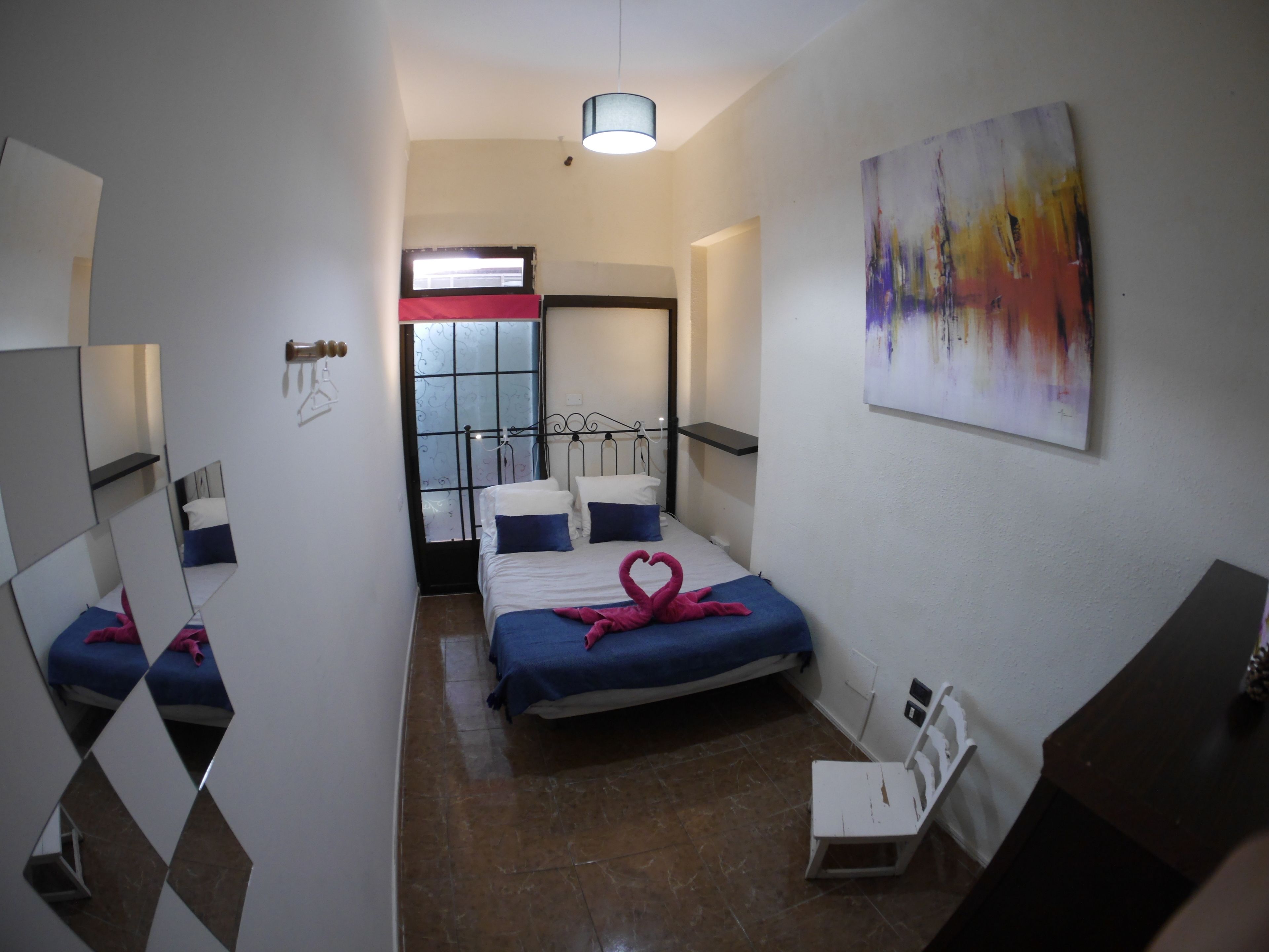 A hotel room with a bed, a chair, a desk, a painting, a window, and a door.