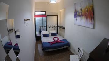 A hotel room with a bed, a chair, a desk, a painting, a window, and a door.