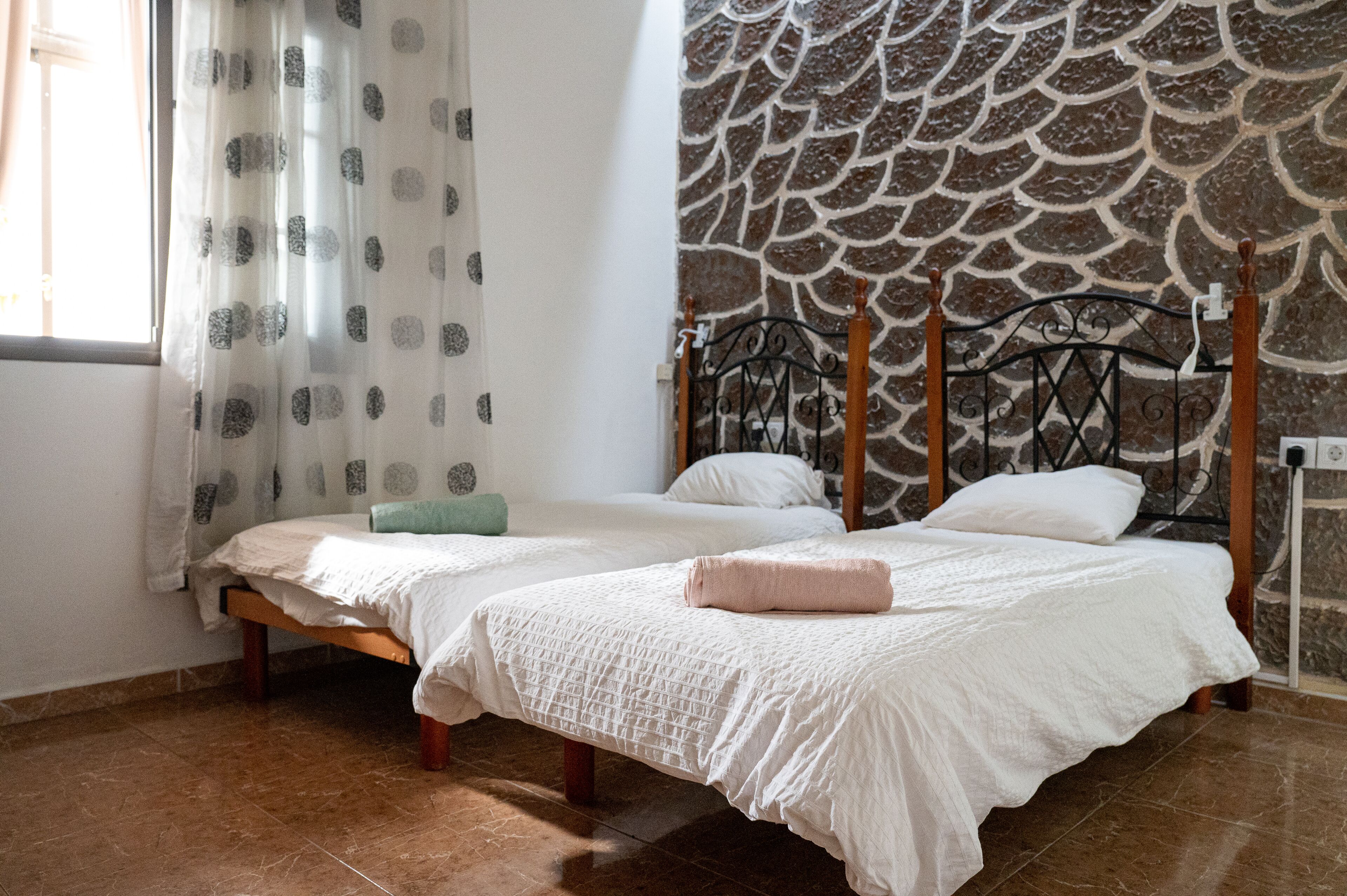 Un dormitorio con dos camas, una pared de piedra y una ventana con cortinas.