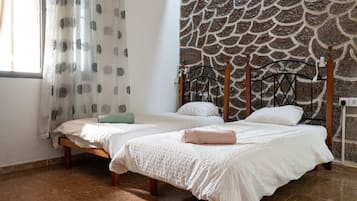 Un dormitorio con dos camas, una pared de piedra y una ventana con cortinas.