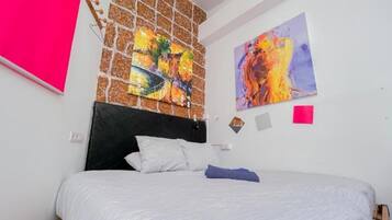 Un dormitorio con cama, cabecera y dos cuadros en la pared.