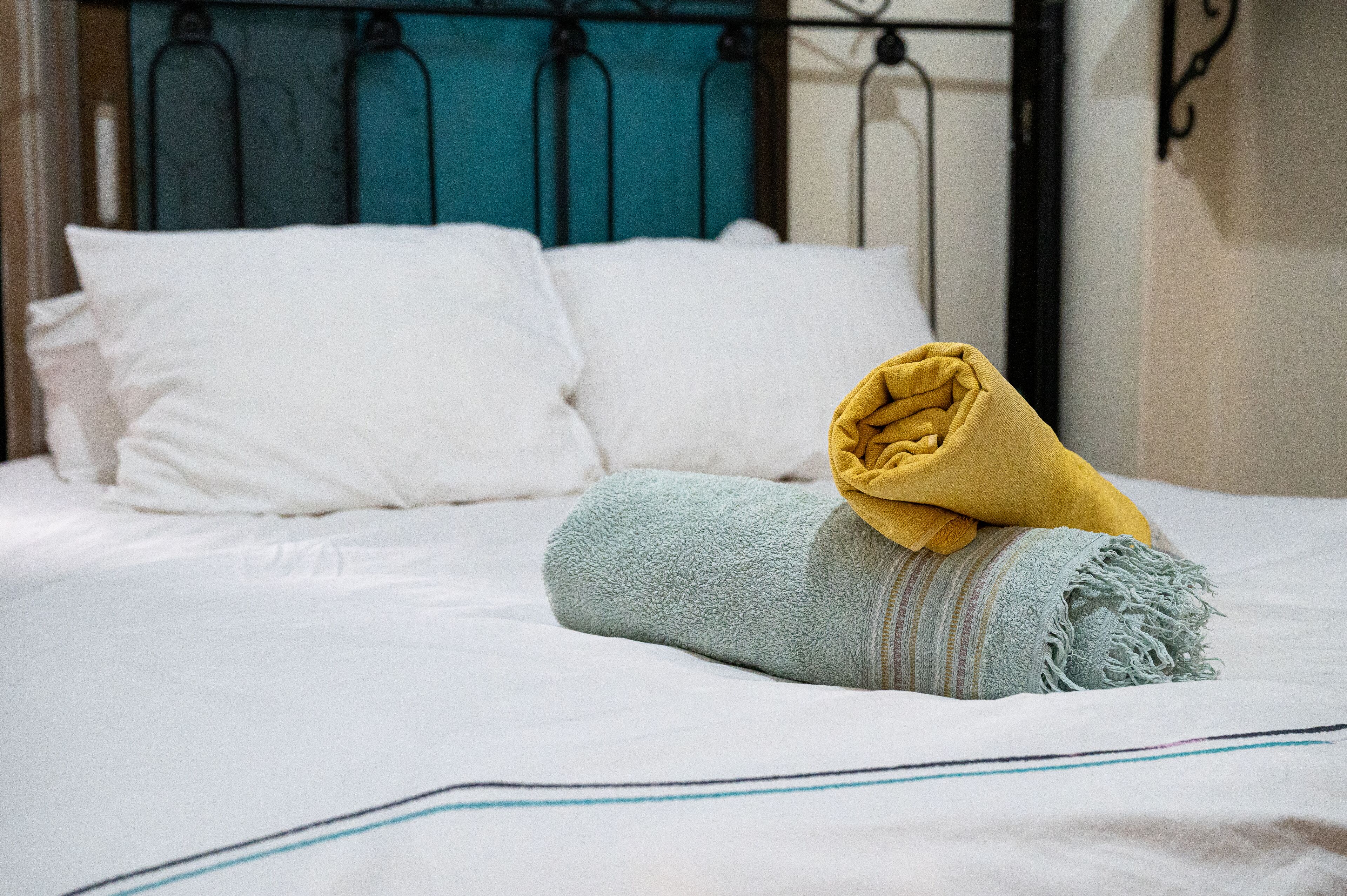Un lit bien fait, avec du linge de lit blanc et une serviette jaune enroulée posée sur le dessus.