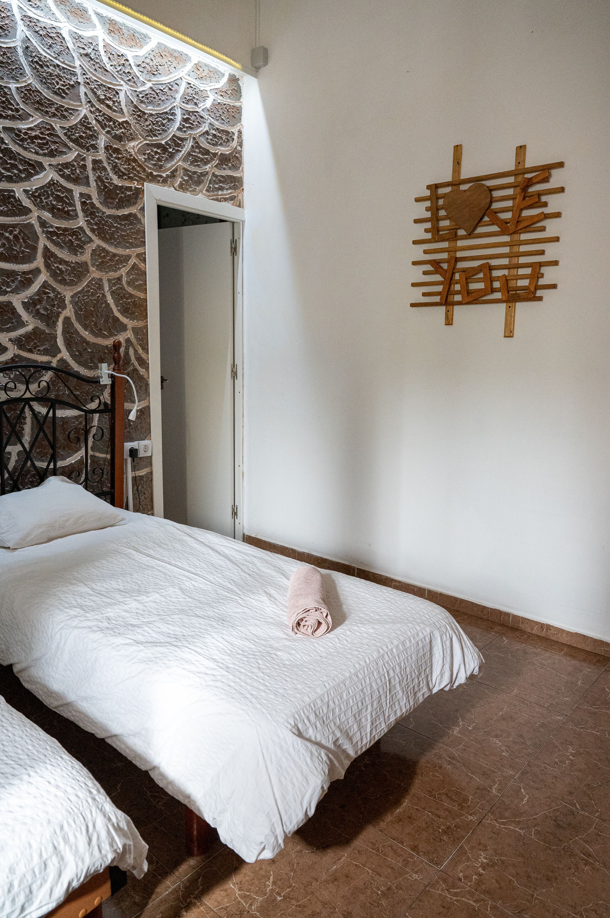 Un dormitorio con dos camas, una pared con diseño de piedra, una obra de arte de madera y suelo de baldosas.