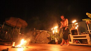 Una persona actuando con accesorios de fuego en un entorno exterior con una estructura de piedra y plantas en macetas.