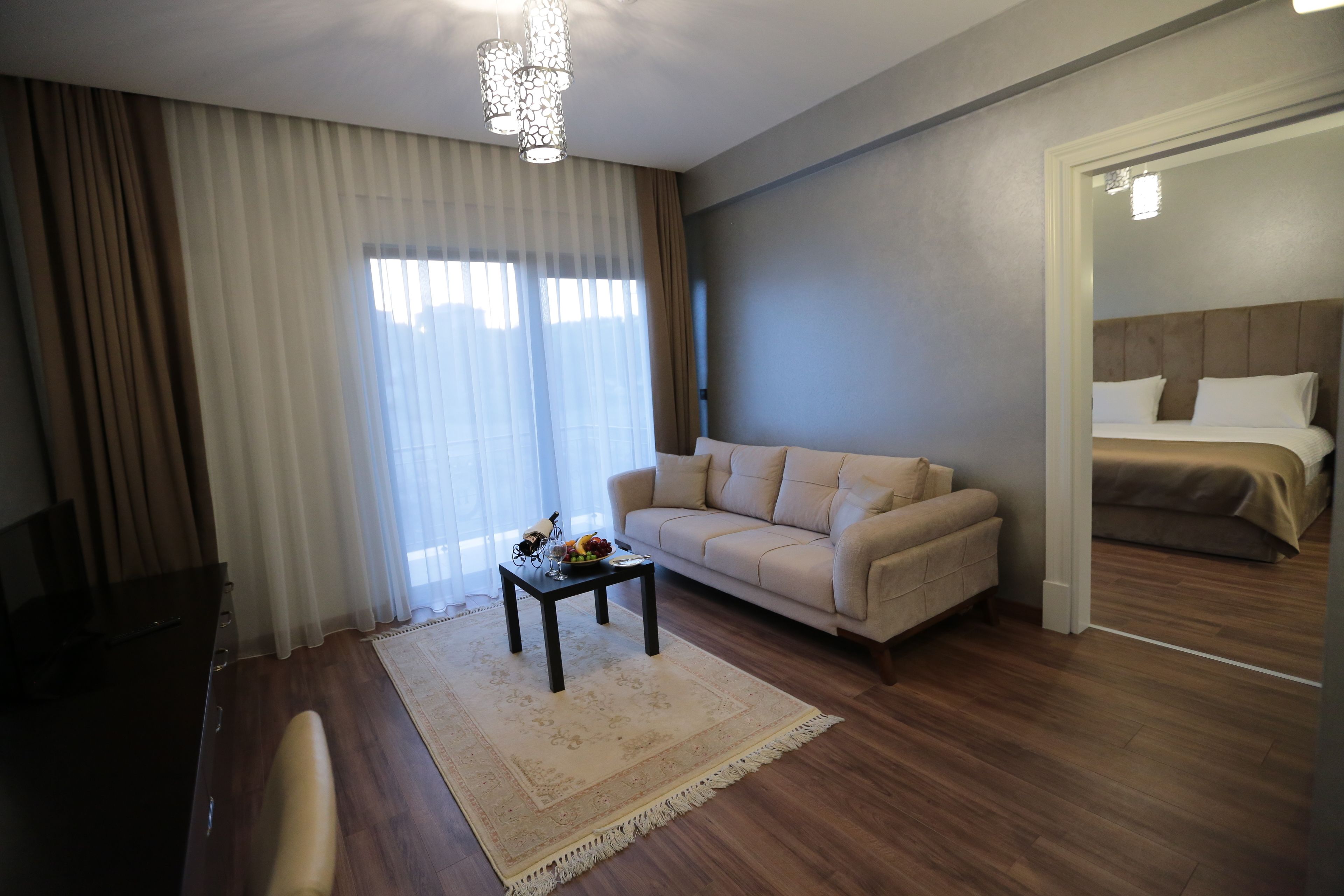 A hotel room with a sofa, a small table with fruit, a wooden floor, and a bed with a headboard.