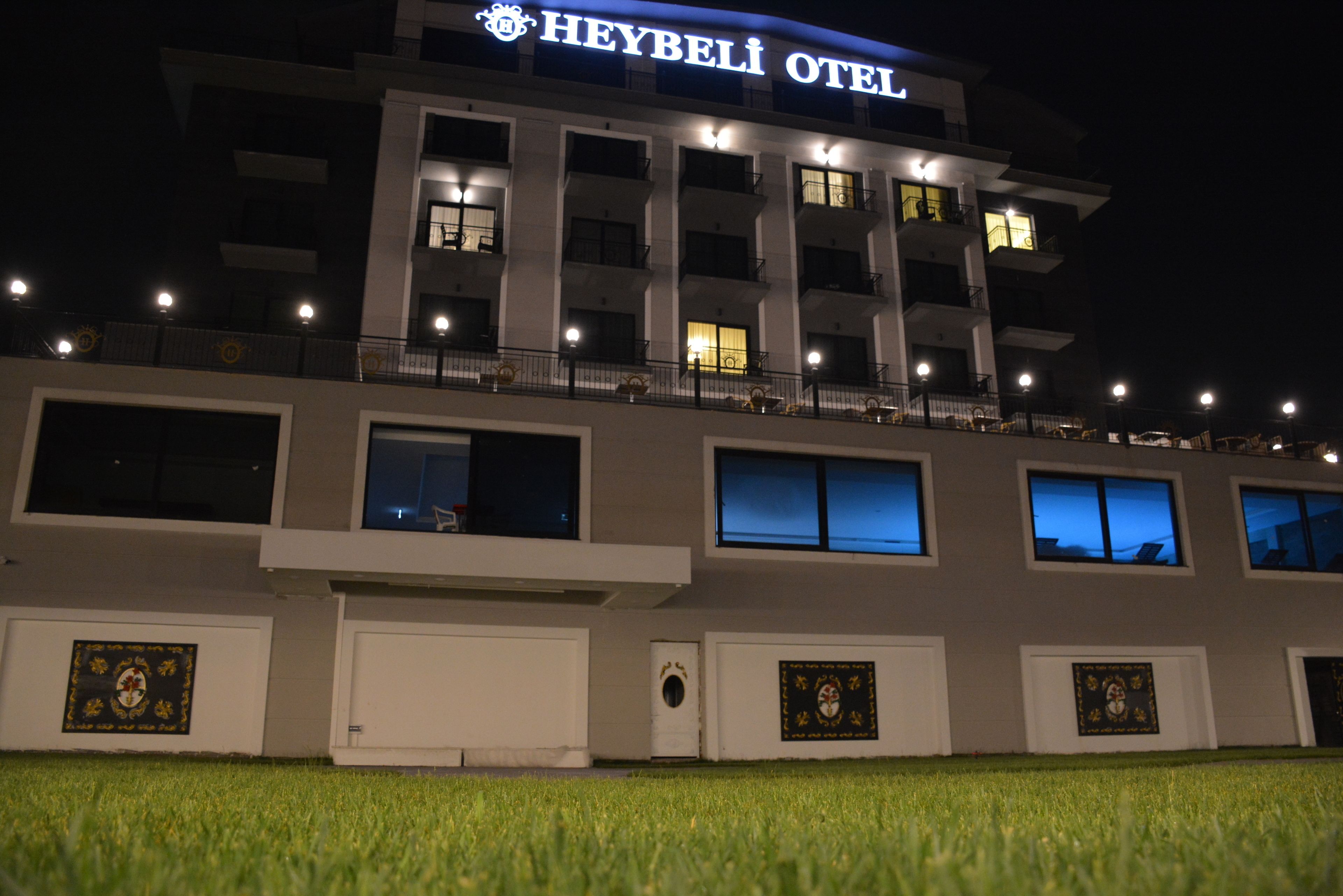 A multi-story hotel with a prominent "Heybelı Otel" sign, large windows, and a well-lit facade.