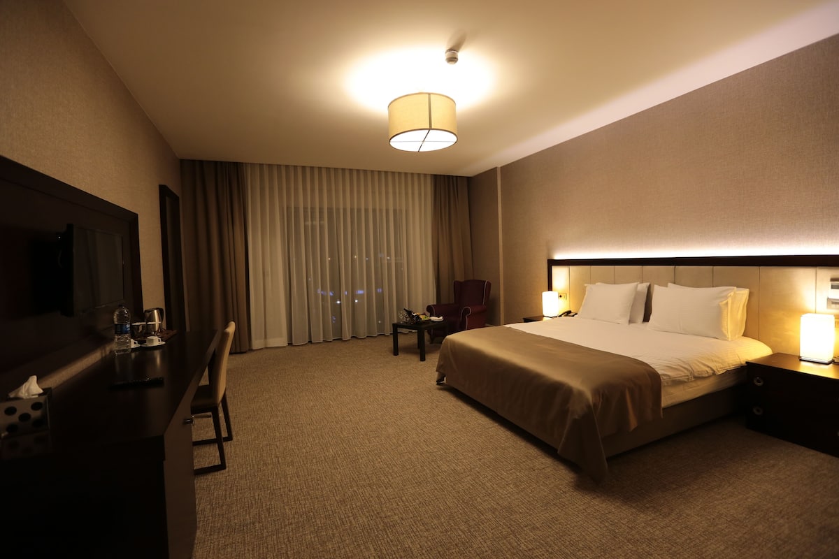 A hotel room with a large bed, a desk with a chair, a TV, and a window with curtains.