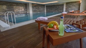 Zona junto a la piscina con una mesa de madera, una botella y un plato de frutas.