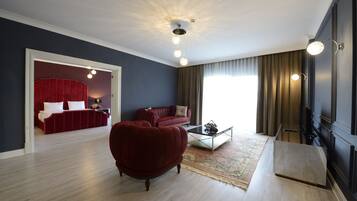 A modern living room with a red sofa, a coffee table, and a red armchair. There is a large window with curtains, a ceiling light fixture, and a flat-screen TV mounted on the wall.