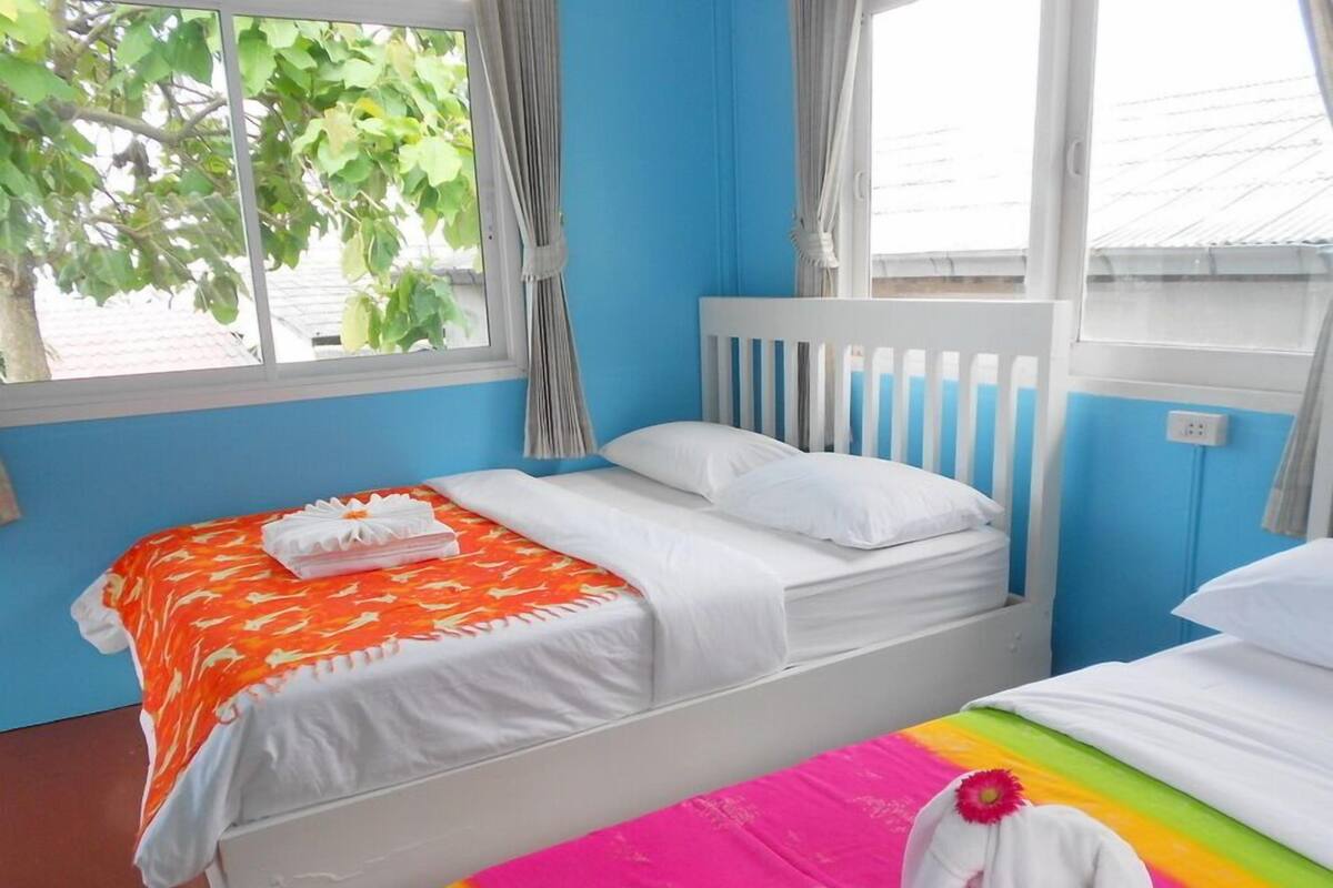 A room with a bed, a window with curtains, and a view of greenery outside.