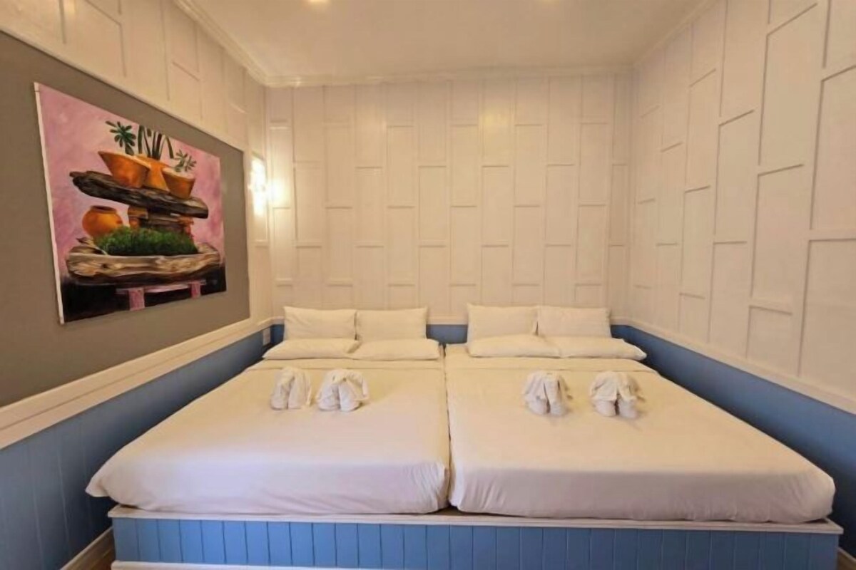 A hotel room with two beds, a painting on the wall, and a blue accent wall.