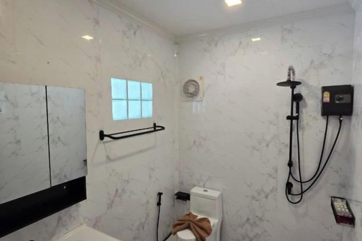 Un baño con pared de mármol, una ventana, inodoro, ducha y toallero.