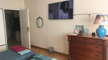 Quarto com cama, cômoda, espelho, televisão e lixeira.