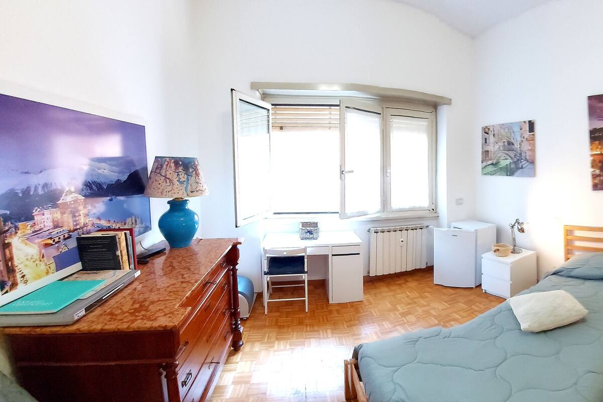A bedroom with two single beds, a desk with a chair, a radiator, and a window.