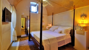 A four-poster bed with a canopy, a television mounted on the wall, and a bedside table with a lamp. - Biomasseria Muto (Ruffano)