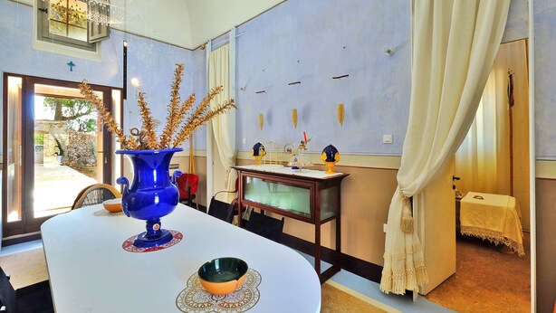 A dining area with a round table, a blue vase, and a bowl on a doily. - Biomasseria Muto (Ruffano)