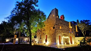 A stone building with a prominent tower, outdoor seating, and a well-lit patio area. - Biomasseria Muto (Ruffano)