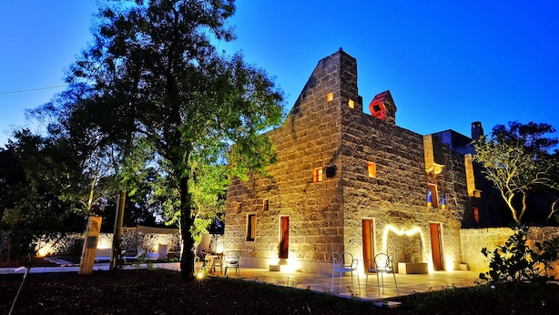 A stone building with a prominent tower, outdoor seating, and a well-lit patio area. - Biomasseria Muto (Ruffano)