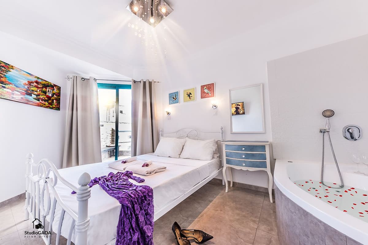 Une chambre à coucher comprenant un lit, une coiffeuse, une baignoire et une fenêtre avec des rideaux.
