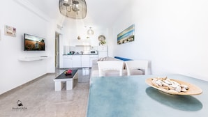 A modern living room with a dining area, a kitchen in the background, and a large window. - Kings Towers Suite Apartments (Tiberias)