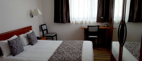 Habitación de hotel con dos camas, un escritorio, una silla y una lámpara.