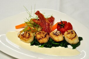 A plate of food with seared scallops, bacon, carrots, and a tomato on a white plate.