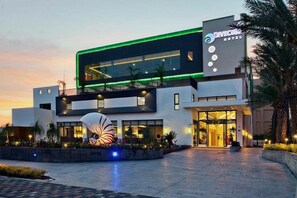 A modern hotel with a prominent green-lit entrance, a large decorative sculpture in front, and a clear sky at dusk. - DiveCube Hotel (Taichung)