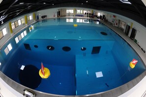 A large indoor swimming pool with multiple lanes, safety equipment, and a lifeguard stand. - DiveCube Hotel (Taichung)