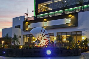 A modern hotel with a large decorative shell sculpture in the courtyard, a second-story balcony with green lighting, and a well-lit entrance. - DiveCube Hotel (Taichung)