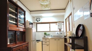 Una cocina compacta con armarios de madera, un microondas integrado, un refrigerador, un lavamanos y un reloj en la pared.