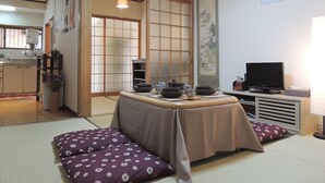 Una habitación japonesa tradicional con suelo de tatami, una mesa baja con un juego de té, un televisor y una puerta corredera.