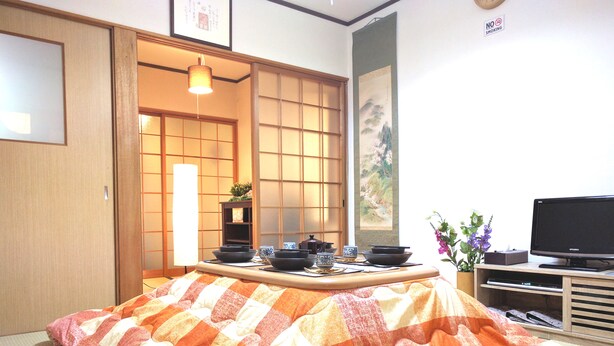 Una habitación japonesa tradicional con suelo de tatami, una mesa baja con utensilios para la ceremonia del té, un televisor y un puertas correderas.