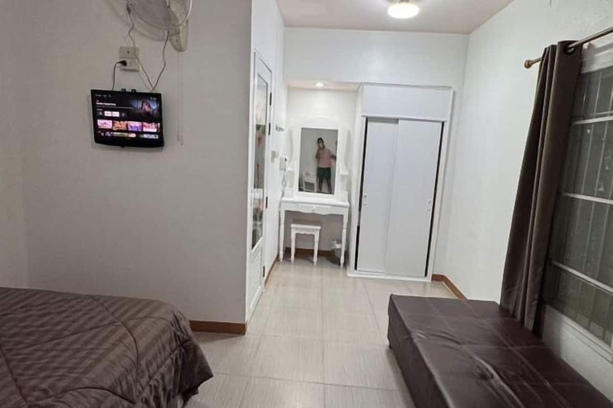 A bedroom with a bed, a TV mounted on the wall, a desk, and a wardrobe.
