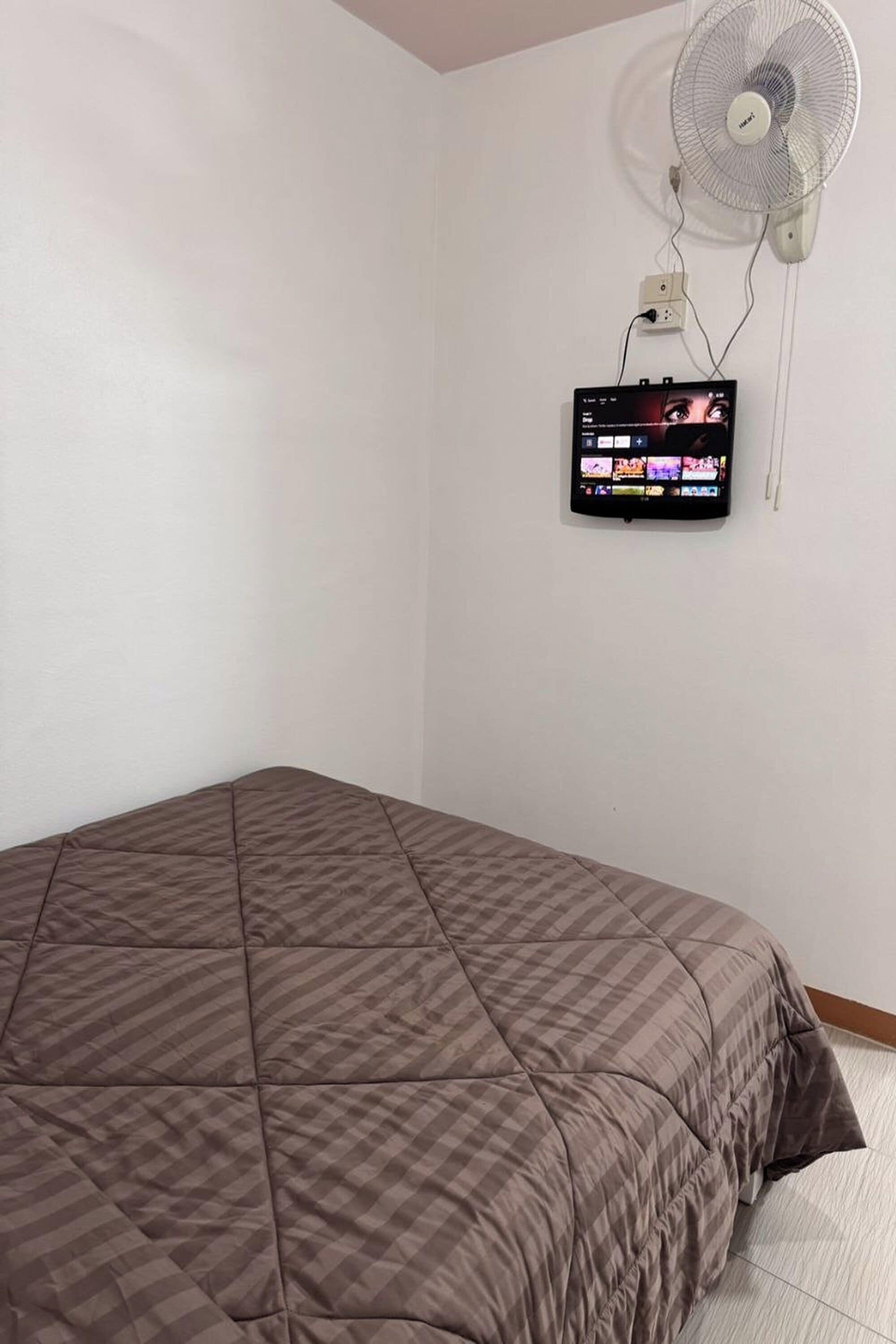 A room with a bed, a wall-mounted TV, and a standing fan.