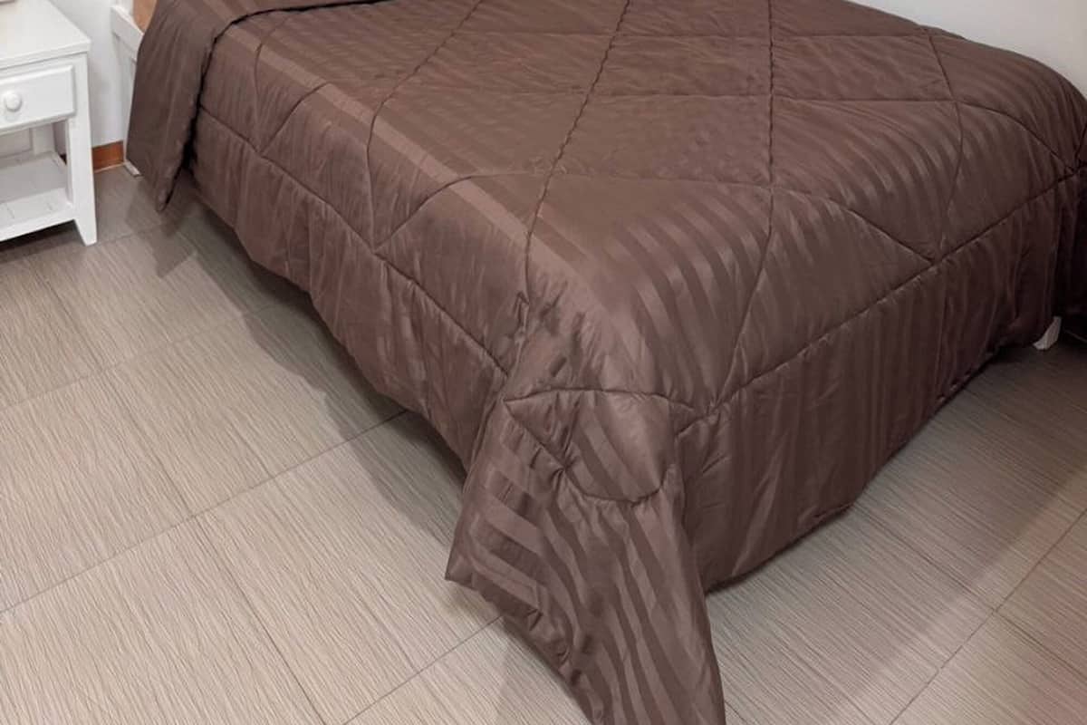 A bedroom with a bed, a nightstand, and a window with blinds.