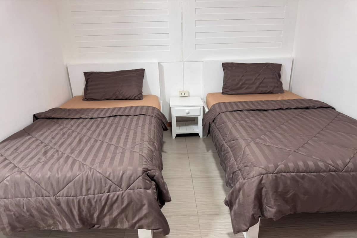 A twin room with two single beds, each with a brown duvet and matching pillows. There is a small bedside table with a lamp between the beds.
