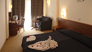 A hotel room with a bed, a desk with a television, a chair, a small table, and curtains.