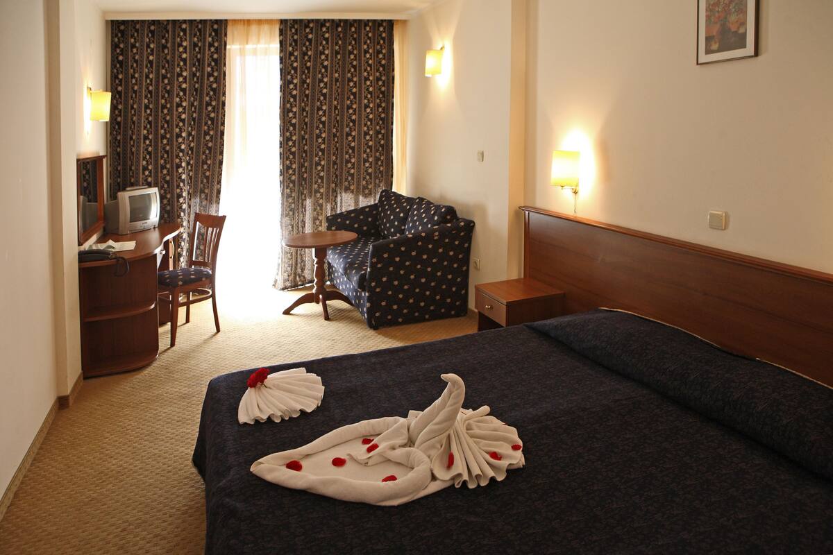 A hotel room with a bed, a desk with a television, a chair, a small table, and curtains.