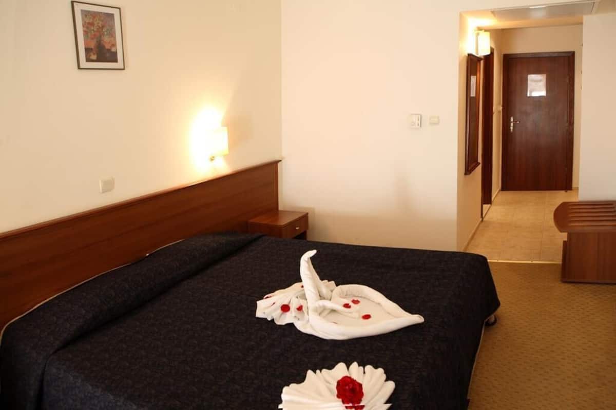 A hotel room with a neatly made bed, a bedside table, a lamp, and a door leading to another room.